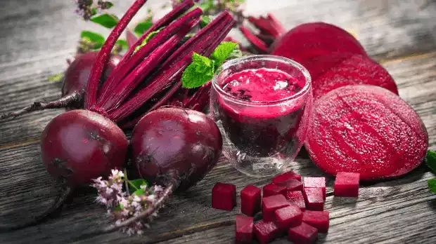 Sur cette image on voit de la betterave sous plusieurs formes : brute, smoothie, cube et en rondelle sur une table en bois.